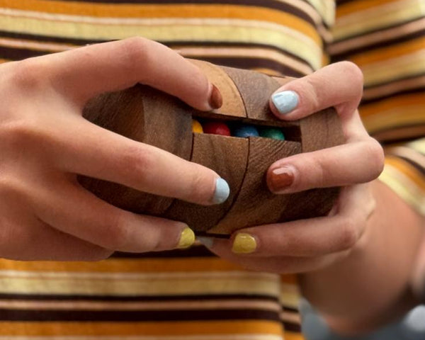 Person wearing a striped shirt holding a wooden object with colorful beads.