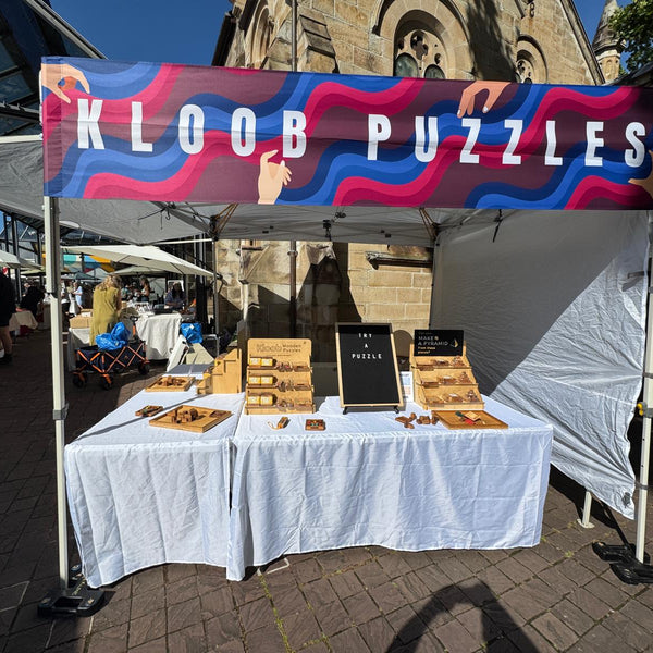 KLOOB PUZZLES booth at an outdoor event with a colorful banner and table displaying puzzles.