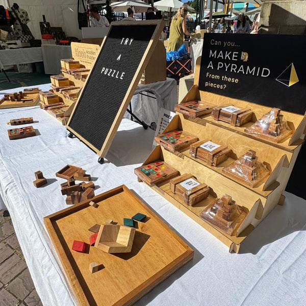 Wooden puzzle display on a table with promotional signs at an outdoor event.