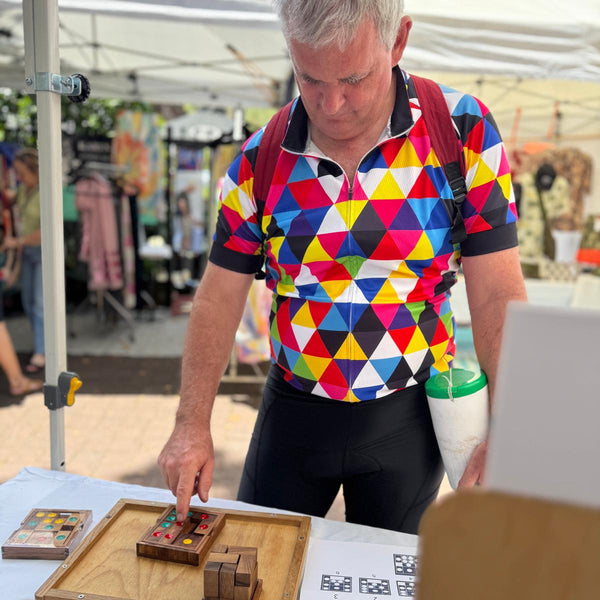 Man in a colorful geometric-patterned shirt playing with wooden puzzle at an outdoor event.