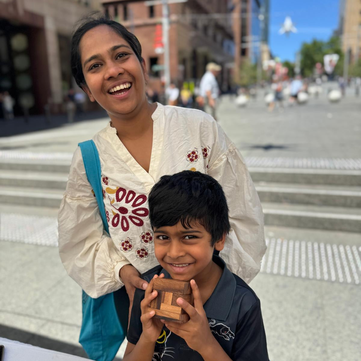 Woman and child holding wooden toys outdoors with a cityscape background